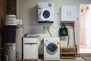 A laundry room with a washing machine, dryer, and stacked laundry baskets. - Oceans 1, Beach Views, 3-Min Walk to Birubi Beach (Anna Bay)