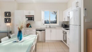 A modern kitchen with white cabinetry, a dishwasher, a microwave, and a coffee maker. - Oceans 1, Beach Views, 3-Min Walk to Birubi Beach (Anna Bay)