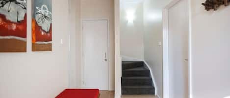 A hallway with a bench, a staircase, and artwork on the walls.