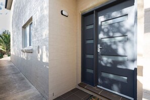 A modern building with a grey facade, a dark blue door, and a small window. - Oceans 1, Beach Views, 3-Min Walk to Birubi Beach (Anna Bay)