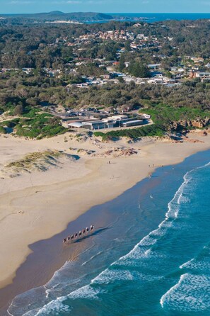Vue aérienne d’une zone côtière comprenant une plage, un petit village et un grand ensemble de bâtiments.
