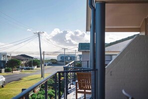 A residential area with a balcony, a chair, and a view of a street with houses and a distant mountain. - Oceans 2, Ocean Views, 3-Min Walk to Birubi Beach (Anna Bay)