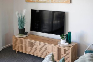 A wooden TV stand with a flat-screen TV mounted above it, a small potted plant, and decorative vases. - Oceans 2, Ocean Views, 3-Min Walk to Birubi Beach (Anna Bay)