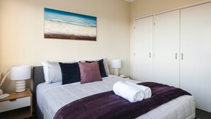 Ein Hotelzimmer mit Bett, Nachttisch, Lampe, Kleiderschrank und einem Bild an der Wand.