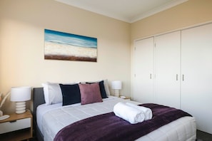 Ein Hotelzimmer mit Bett, Nachttisch, Lampe, Kleiderschrank und einem Bild an der Wand.