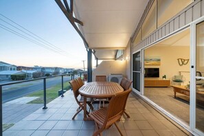 Un pati exterior modern amb una taula rodona i seients, una porta corredissa de vidre que dona a un espai de vida, i vista a un carrer residencial.
