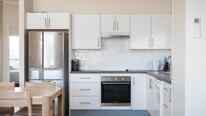 Eine moderne Küche mit weißen Schränken, einem Edelstahlkühlschrank, einem Einbauofen und einem Essbereich mit einem Holztisch und Stühlen.