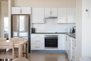 Eine moderne Küche mit weißen Schränken, einem Edelstahlkühlschrank, einem Einbauofen und einem Essbereich mit einem Holztisch und Stühlen.