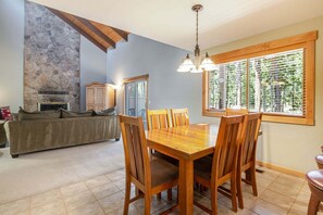 A dining area with a wooden table and chairs, a stone fireplace, and a window with blinds. - 4 Virginia Rail - Dog-Friendly Sunriver Home with A/C, Hot Tub & SHARC Passes (Sunriver)