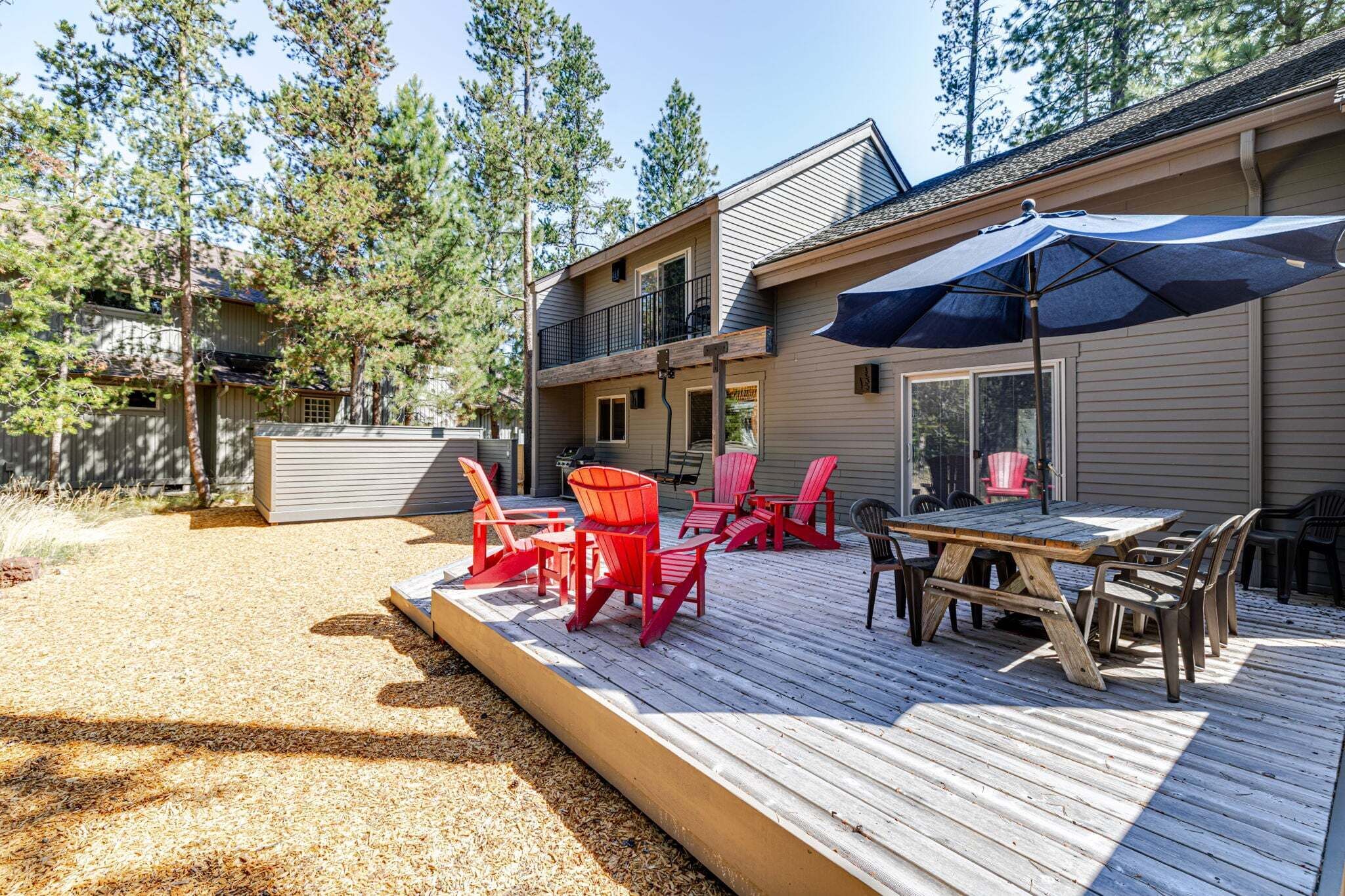 A deck with outdoor furniture, a covered area, and a two-story building with a balcony.