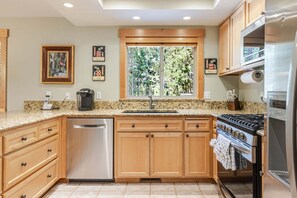 A kitchen with wooden cabinets, a stainless steel dishwasher, a gas stove, and a window with a view of trees. - 4 Virginia Rail - Dog-Friendly Sunriver Home with A/C, Hot Tub & SHARC Passes (Sunriver)