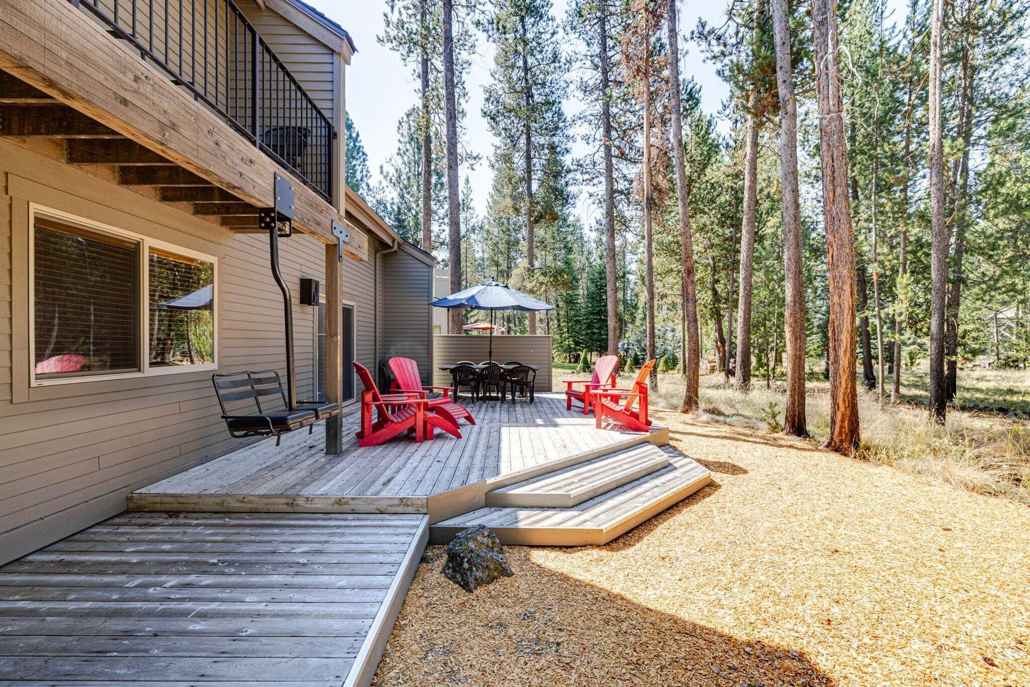 A wooden deck with outdoor furniture, a covered patio area, and a forested backdrop.