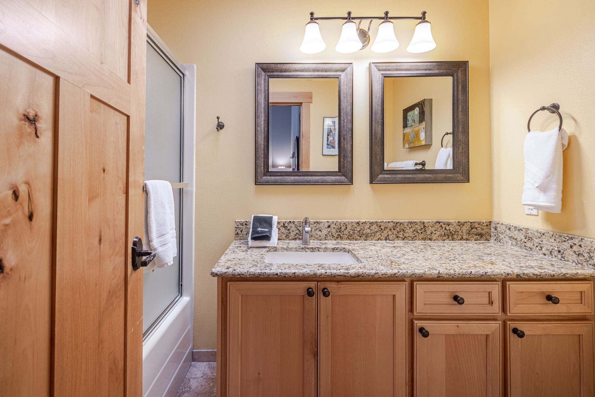 A bathroom with wooden cabinets, a granite countertop, a sink, a mirror, and a towel rack.