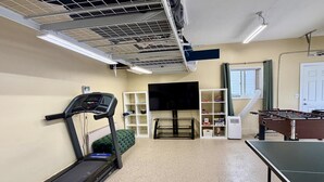 A room with a treadmill, a television, a foosball table, and a window with curtains. - Sunshine House | Bright & Cozy Getaway for Families, Friends, and Relaxation (Rexburg)
