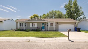 A single-story house with a front porch, a garage, and a well-maintained lawn. - Sunshine House | Bright & Cozy Getaway for Families, Friends, and Relaxation (Rexburg)