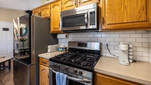 A kitchen with wooden cabinets, a stainless steel refrigerator, a microwave, a stove, and a coffee maker. - Sunshine House | Bright & Cozy Getaway for Families, Friends, and Relaxation (Rexburg)