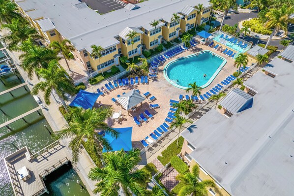 Ein Luftbild zeigt ein Resort mit Schwimmbad, Liegestühlen und Palmen.