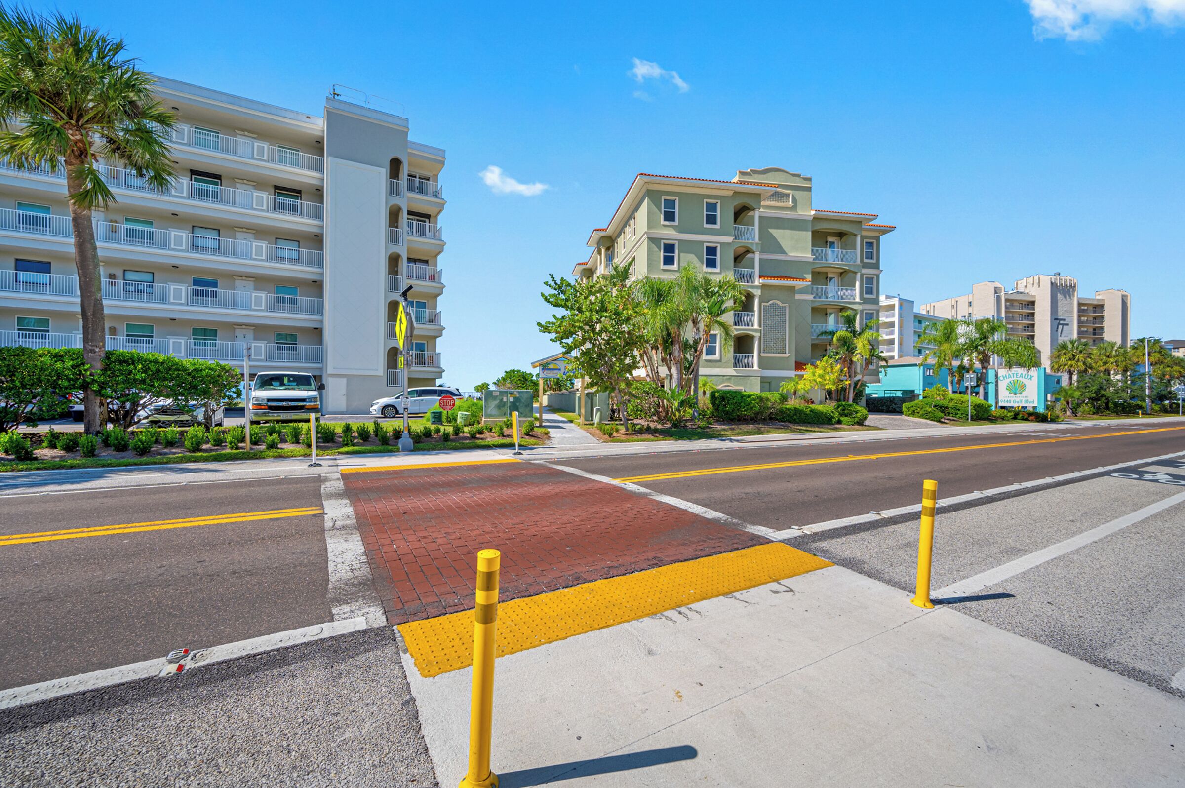 A multi-story hotel with balconies, a parking area, and a pedestrian crossing.