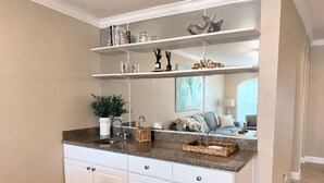 Una cucina con mobili bianchi, piani di lavoro in granito e un ripiano sospeso sopra il lavello.
