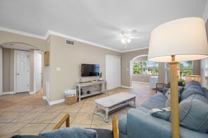 A living room with a television, sofa, and a ceiling fan. - 👣Barefoot Beach Resort #E211 - 2 Bedroom condo in Indian Shores Beach with a Pool!🩴 (Indian Shores)