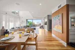 A modern living room with a dining area, large windows, and a view of the outdoors. - Alex Headland Haven - 3 Level Modern Retreat (Mooloolaba Region)