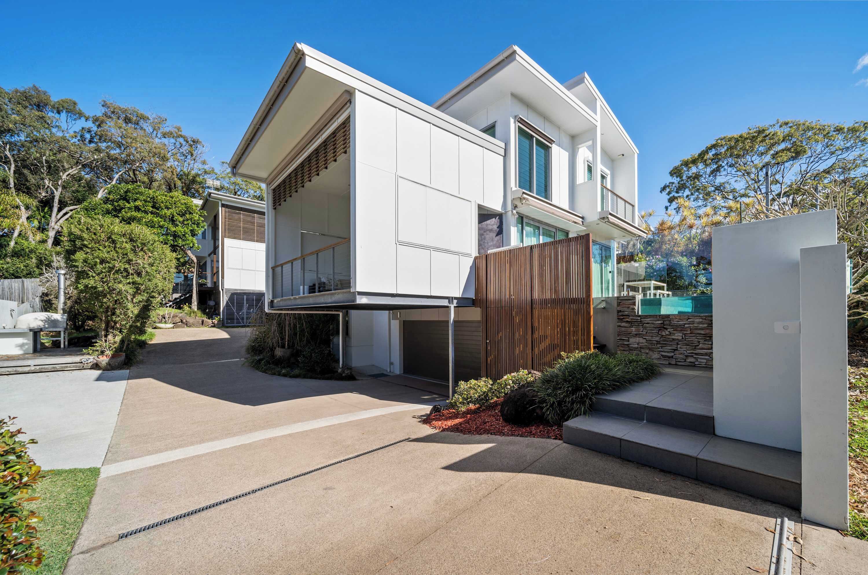 Een modern huis met twee verdiepingen, een garage, een overdekte oprit en een stenen muur.