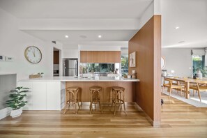Een moderne keuken met een centraal eiland, houten barstoelen en een eethoek met een houten tafel en stoelen.