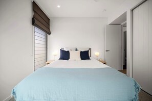 A bedroom with a large bed, two bedside lamps, a window with blinds, and a door leading to another room. - Alex Headland Haven - 3 Level Modern Retreat (Mooloolaba Region)