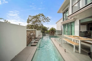 Un espace piscine extérieur moderne, agrémenté d’un mur en pierre, d’une terrasse en bois et d’une table à manger avec des bancs.