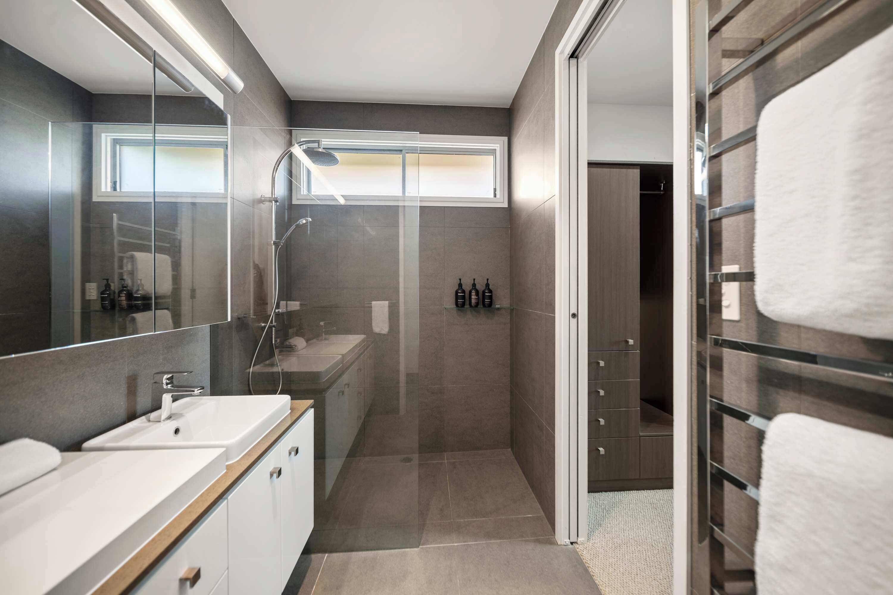 A modern bathroom with a glass shower enclosure, a vanity with a sink, and a walk-in closet with hanging towels.