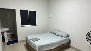 Ein Schlafzimmer mit einem Einzelbett, einem Fenster, einem Nachttisch und einem Wandventilator.