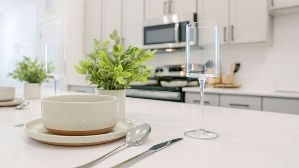A modern kitchen with white cabinets, a microwave, and a dining table set with a bowl, a glass, and cutlery. - Homey Worker-Friendly 2BR I Pool & Gym (Sherman)