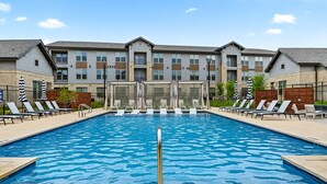 A swimming pool with lounge chairs and umbrellas, surrounded by a building with multiple windows and balconies. - Homey Worker-Friendly 2BR I Pool & Gym (Sherman)