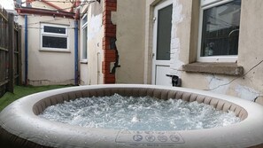 Una bañera de hidromasaje inflable en un patio trasero con un muro de ladrillo y una ventana.