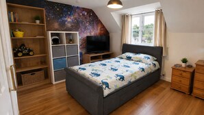 A bedroom with a bed, a TV, a bookshelf, a dresser, and a window with curtains. - Spacious Detached 4-Bedroom Family Home with Large Garden (Worminghall)