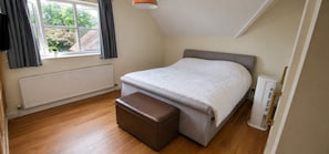 A bedroom with a bed, a radiator, a window with curtains, and a bedside table.