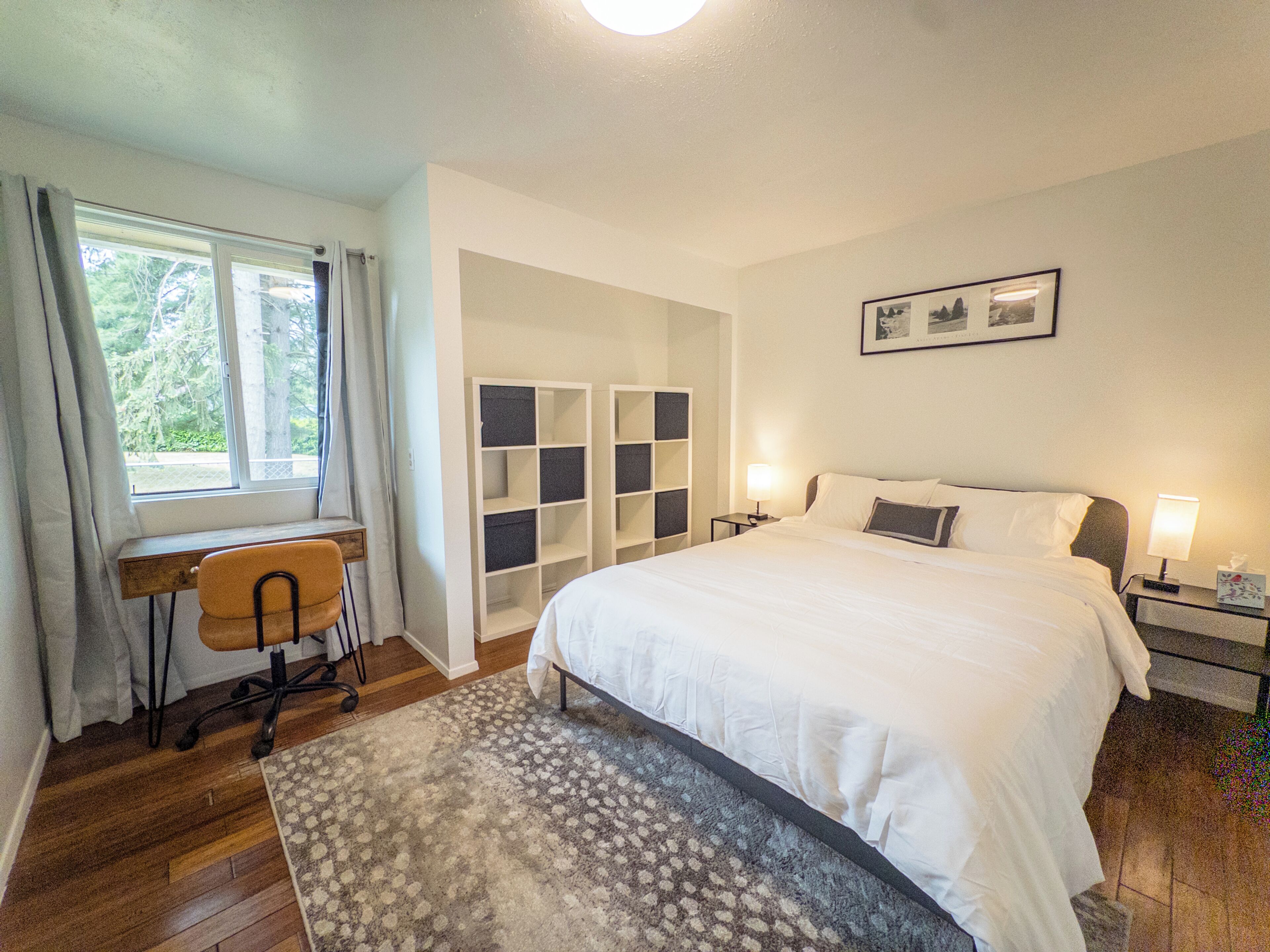 A bedroom with a bed, a desk, a chair, and a window with curtains.