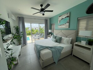 A modern hotel room with a bed, a ceiling fan, a view of the pool, and a painting on the wall. - Sosua Ocean Village Luxury Villa: 3BR/3.5BA Pool Oasis (Sosúa)