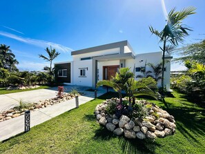 A modern two-story house with a well-maintained lawn, a stone pathway, and tropical plants. - Sosua Ocean Village Luxury Villa: 3BR/3.5BA Pool Oasis (Sosúa)