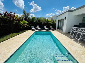 A rectangular swimming pool with clear blue water, surrounded by a tiled deck. There are lounge chairs and a bar area with a stone wall backdrop. - Sosua Ocean Village Luxury Villa: 3BR/3.5BA Pool Oasis (Sosúa)