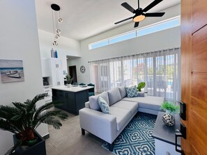 A modern living room with a sofa, a ceiling fan, and a large window with curtains. - Sosua Ocean Village Luxury Villa: 3BR/3.5BA Pool Oasis (Sosúa)