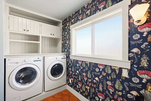 Ein Waschraum mit zwei weißen Waschmaschinen, einem weißen Regalschrank und einem Fenster mit Blick.