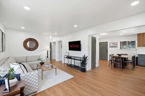 A modern living room with a sofa, coffee table, and a flat-screen TV mounted on the wall. - Family Oasis! Hot Tub Fire Pit Game Room Sleeps 12 (San Diego)