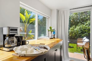 Eine Küche mit einer Kaffeemaschine, einer Schale Marshmallows und Blick auf einen Garten durch große Fenster.