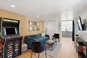 Ein Wohnzimmer mit Spielkonsole, einer Couch, einem Couchtisch und einem Fernseher.