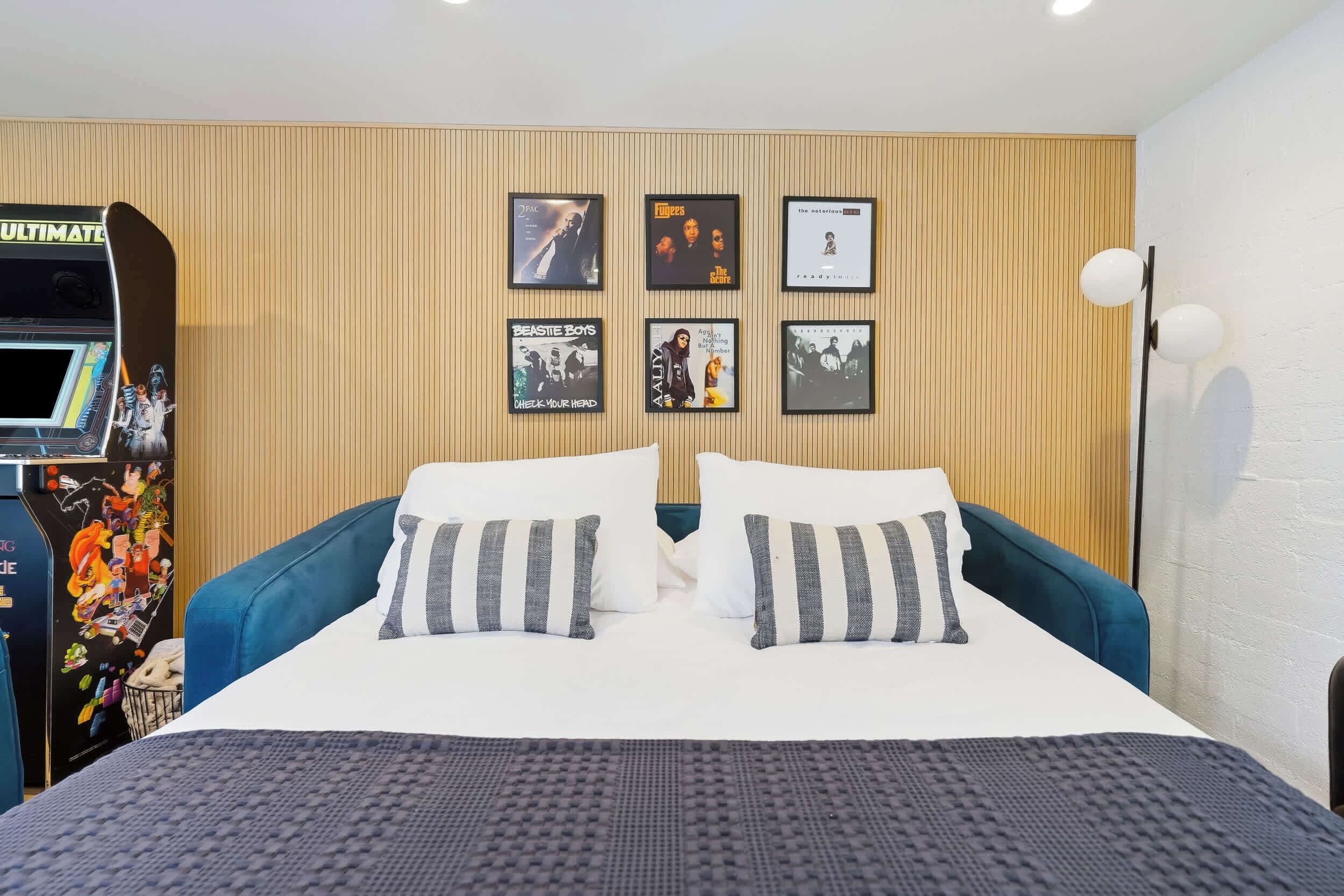 Een hotelkamer met een bed, kussens, een wandtelevisie en lijstjes met elpees.