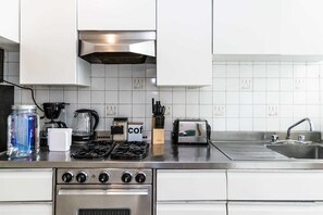 A modern kitchen with white cabinets, a stainless steel stove, a coffee maker, and a toaster. - Beautiful 2 bd apartment in the heart of Condesa (Mexico City)