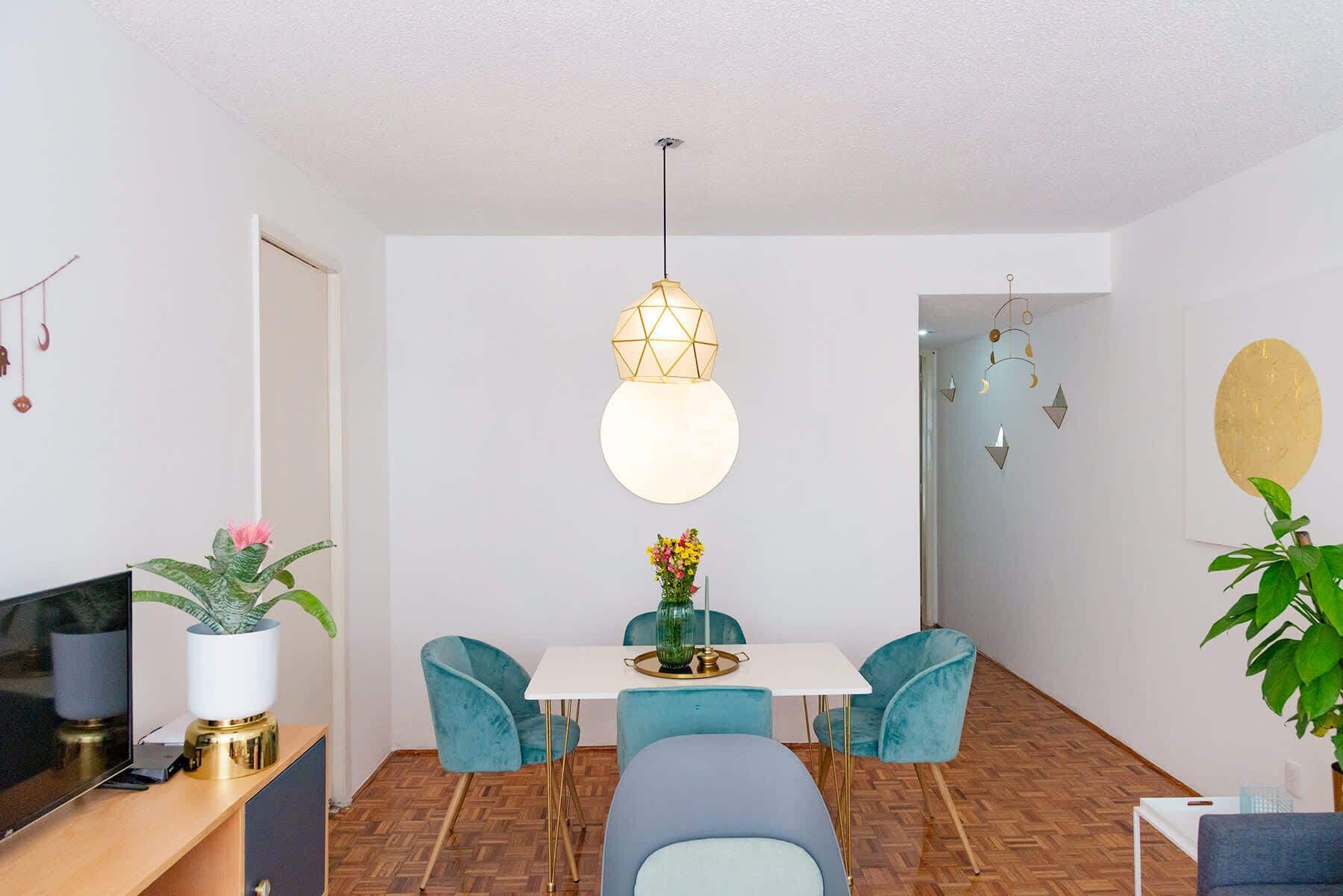 A dining area with a white table, teal chairs, and a hanging light fixture.