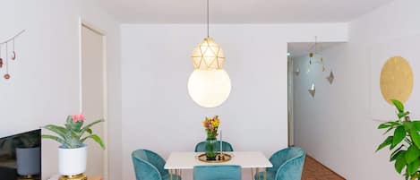 A dining area with a white table, teal chairs, and a hanging light fixture.