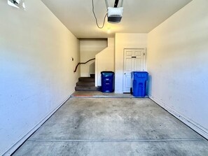 Ein Flur mit Betonboden, einer Treppe und zwei blauen Mülleimern.